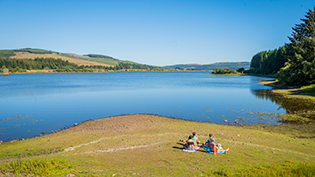 Carron Valley reservoir with group of people sunbathing on the shore